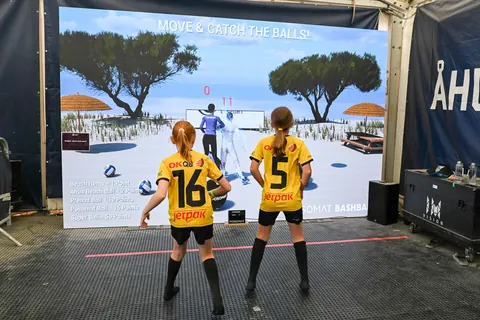 Zwei Kinder in Sportkleidung spielen Bashball vor einer LED-Wand mit Strandmotiv