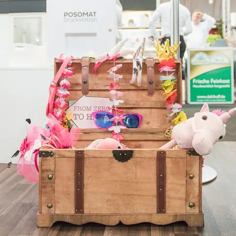 Große Holzkiste voller bunter Verkleidungen und Accessoires neben einer Fotobox