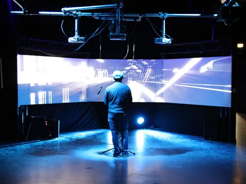 Ein Besucher steht vor einer großen gebogenen Projektionsfläche mit abstrakter 3D-Welt
